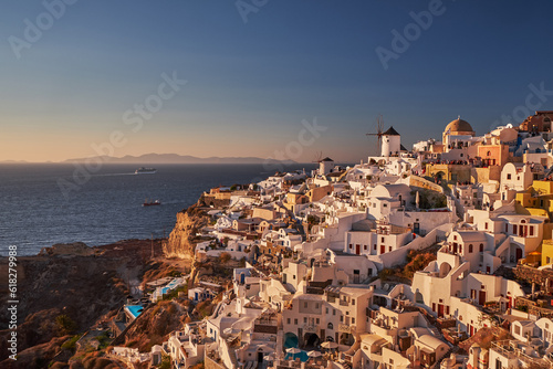 Beautiful view from the old castle of Oia village with traditional white houses and windmills in Santorini island in Aegean sea at sunset, Greece