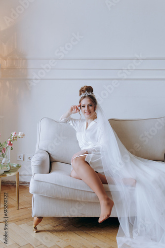 Morning preparations of a beautiful, sexy bride in a bathrobe on the balcony and on the sofa, where she puts on shoes in a wedding dress