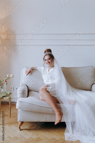 Morning preparations of a beautiful, sexy bride in a bathrobe on the balcony and on the sofa, where she puts on shoes in a wedding dress
