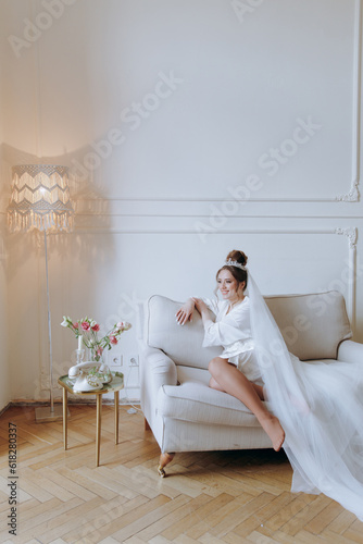 Morning preparations of a beautiful, sexy bride in a bathrobe on the balcony and on the sofa, where she puts on shoes in a wedding dress