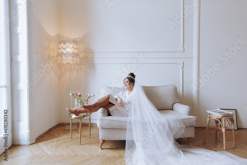Morning preparations of a beautiful, sexy bride in a bathrobe on the balcony and on the sofa, where she puts on shoes in a wedding dress