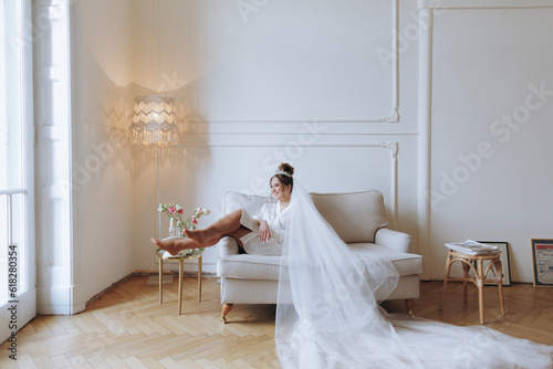 Morning preparations of a beautiful, sexy bride in a bathrobe on the balcony and on the sofa, where she puts on shoes in a wedding dress
