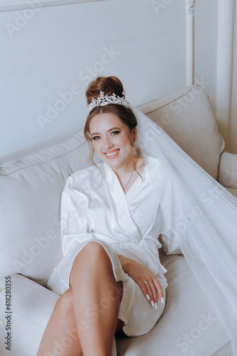 Morning preparations of a beautiful, sexy bride in a bathrobe on the balcony and on the sofa, where she puts on shoes in a wedding dress