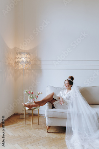 Morning preparations of a beautiful, sexy bride in a bathrobe on the balcony and on the sofa, where she puts on shoes in a wedding dress