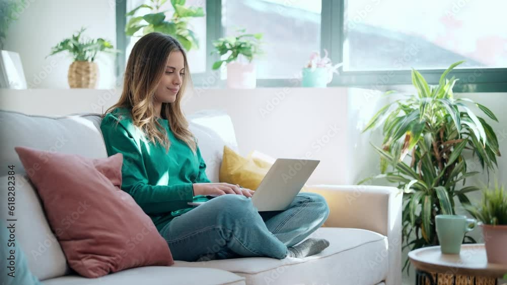 Video of beautiful kind woman working with laptop while sitting on couch in living room at home Video of beautiful kind woman working with laptop while sitting on couch in living room at home
