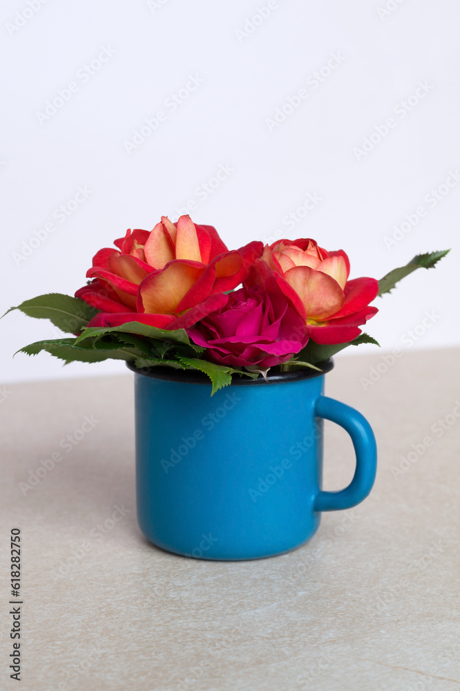 A blue cup filled with flowers: different varieties of pink roses. A small bouquet of garden roses. Beige background. Close up, front view.