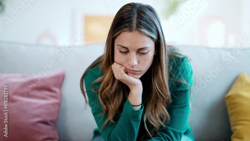 Video of beautiful young woman thinking and worried sitting on couch at home.