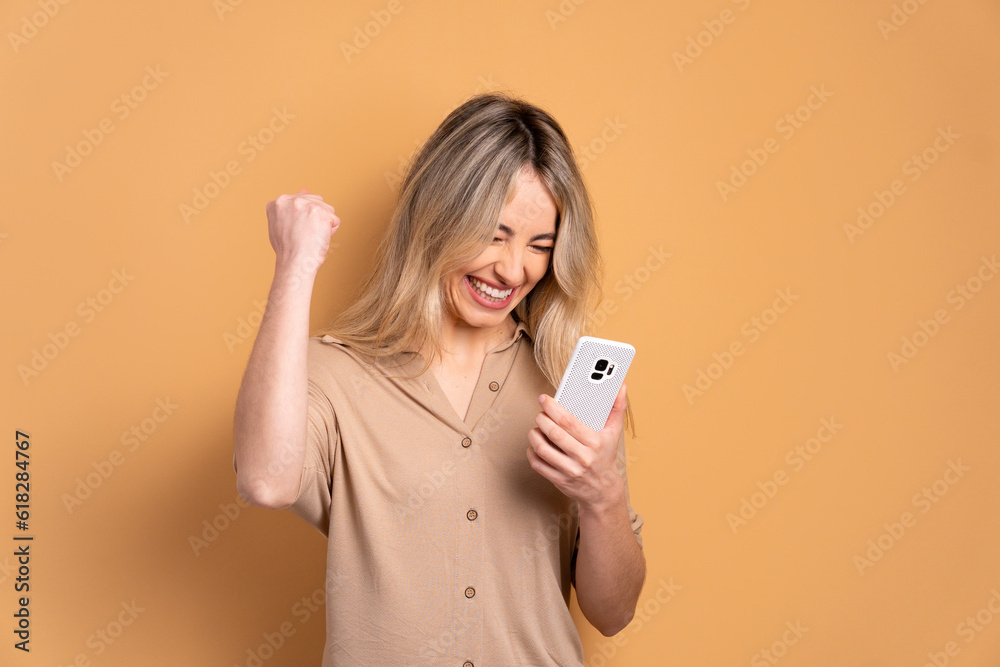 fun young woman raising arms and celebrating in beige background. network, messaging, internet concept. fun young woman raising arms and celebrating in beige background. network, messaging, internet concept.