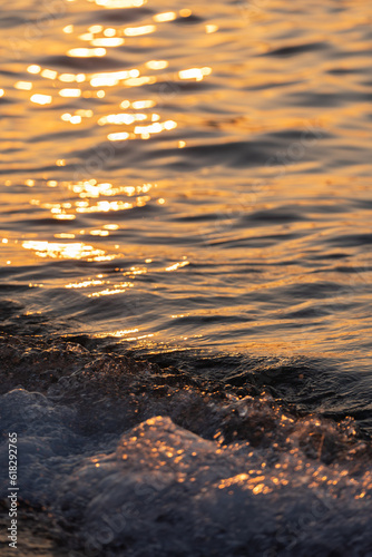 Sea wave splashes close up. Ripple sea ocean water surface with golden sunset light.