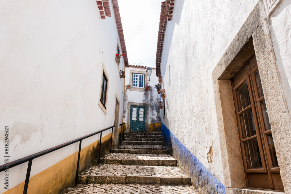 Tight alley in the medieval city of Obidos in west Portugal. White walls with yellow and blue highlights. Small corridor with window rames in an ancient european town. 