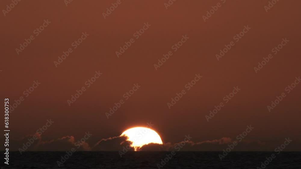 Time lapse of sun rising behind low horizon clouds and into a warm clear sky over water, night to day transition.