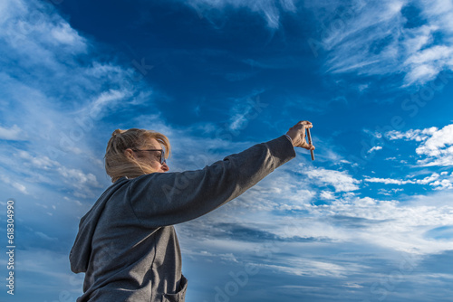 Woman taking selfies with mobile phone outdoors with cloudy blue sky. Technology concept. © fotosdanielgbueno