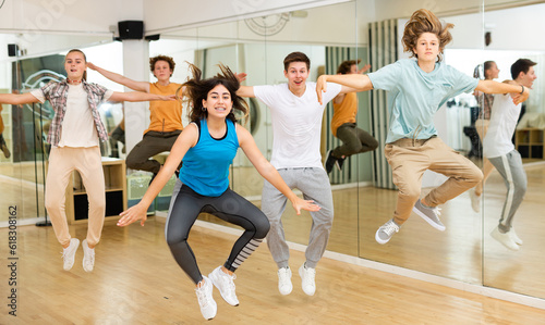 Fototapeta Naklejka Na Ścianę i Meble -  Group of cheerful sportive teenagers training in modern dance hall, jumping together.