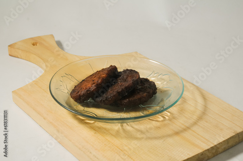 Three pieces of tempe bacem are served on a small plate on a wooden board isolated on a white background. photo