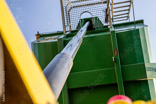 Dynamic perspective view of the hydraulic piston of the green and yellow tilting trailer, agricultural industry.