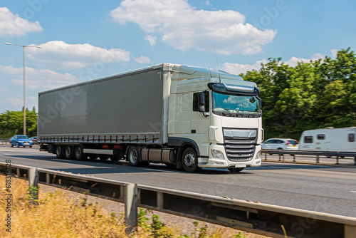 Curtain trailer lorry speeding on the motorway against the blue and cloudy sky.