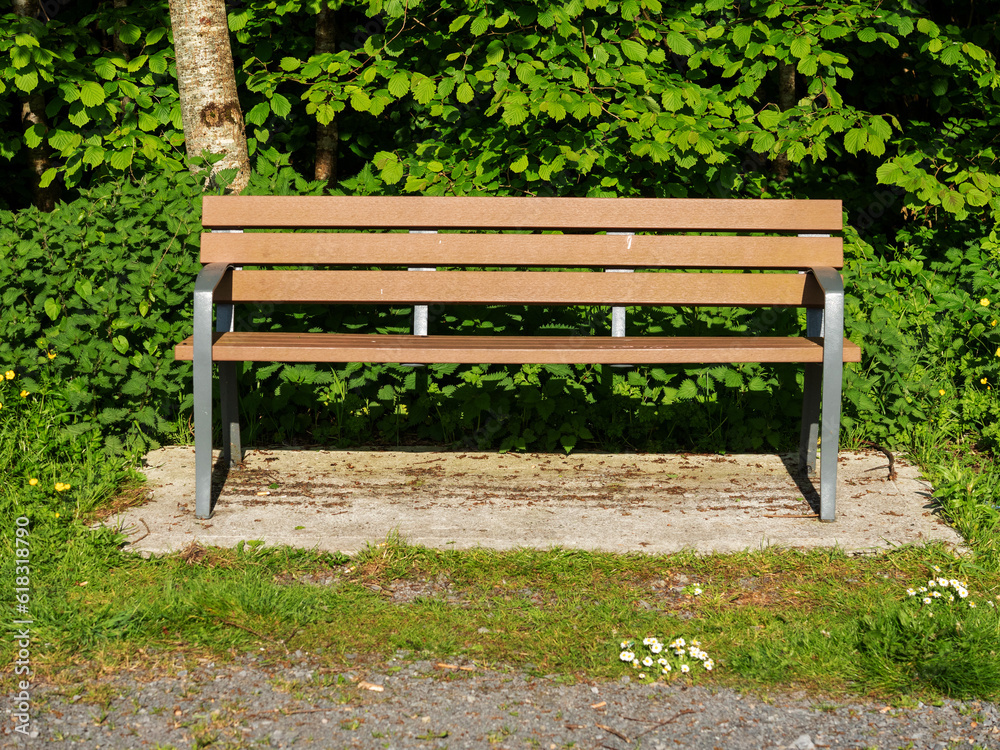 Brown bench in a park on a hot summer day. Metal frame and strong long lasting plastic materials. Park design. Sitting area.