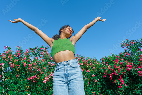 Chica con un día sensacional disfrutando del sol y el ambiente sano de un parque con vegetación y flores a su espalda.