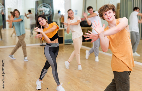 Portrait of positive teenager learning dynamic dance moves with group of teens in choreography class