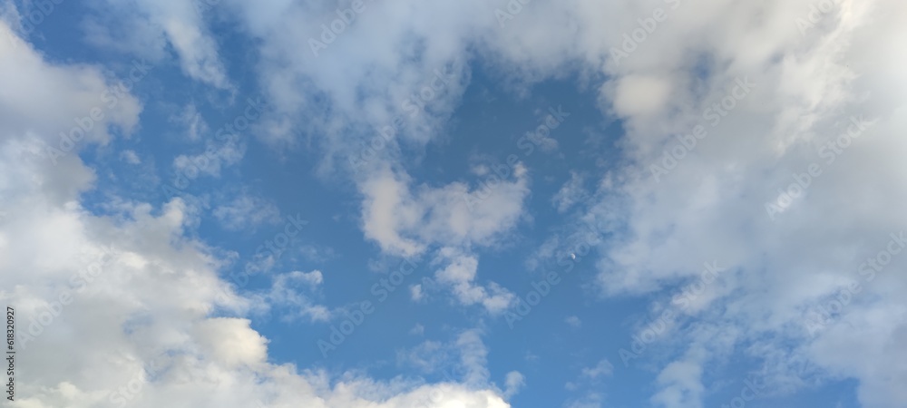 White fluffy clouds. Sunny spring day. White clouds of various shapes and sizes hang high in the sky. Above them is a light blue sky. The clouds are like airy soft cotton wool.