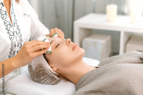 The cosmetologist cleans the face of a beautiful caucasian woman with special disks before applying a mask, peeling, scrub. Facial skin care procedures in a beauty salon. Beauty concept