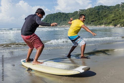 Photography latin surf instructor and two men beginner surfers try to stand up on surfboard