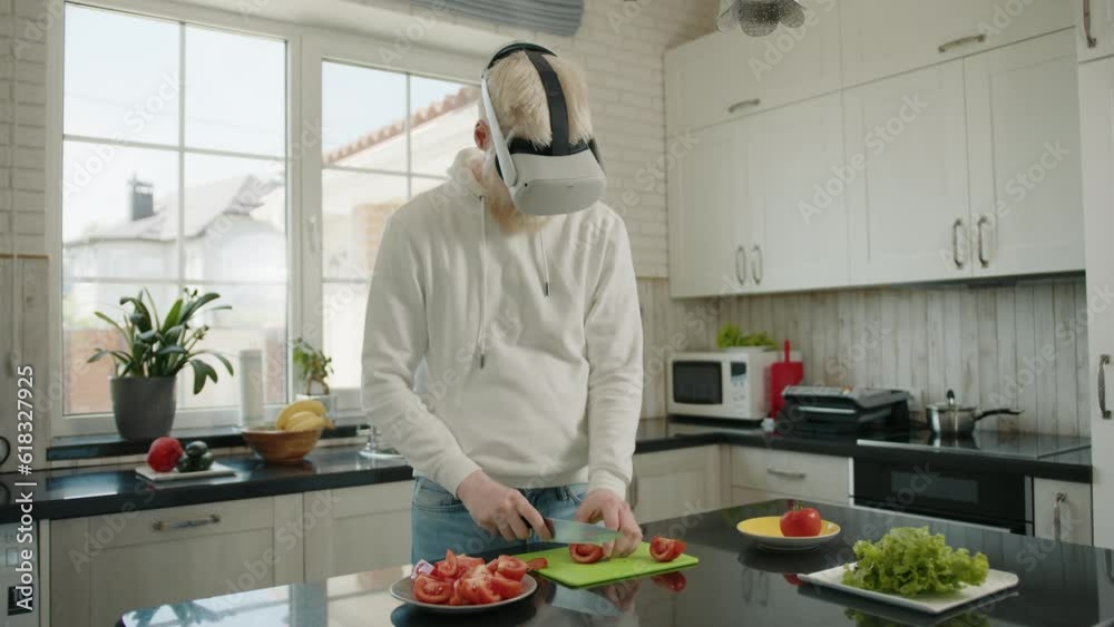 Albino man cutting tomatoes on a cutting board on modern kitchen at home, wearing virtual reality glasses. Digital world. Albino man in VR glasses cooks. High quality 4k footage