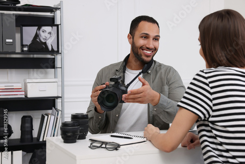 Young professional photographer holding camera while talking with woman in modern photo studio