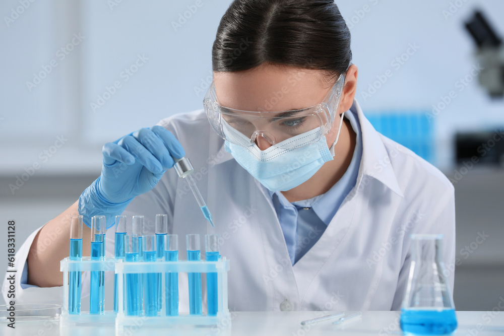Scientist dripping liquid from pipette into test tube in laboratory Scientist dripping liquid from pipette into test tube in laboratory