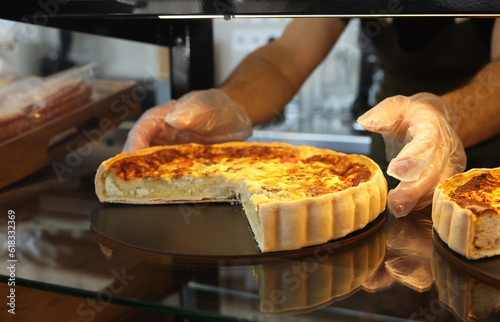 Seller taking tasty quiche from showcase in bakery shop, closeup
