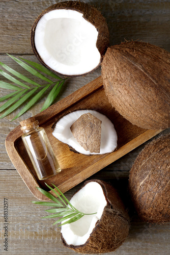 Bottle of organic coconut cooking oil, fresh fruits and leaves on wooden table, flat lay