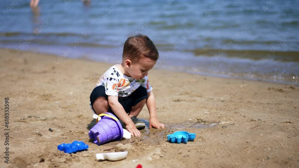 Calm Caucasian toddler squatted on the sea shore. Focused kid plays with sand on sunny day. Calm Caucasian toddler squatted on the sea shore. Focused kid plays with sand on sunny day.