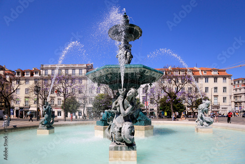 A majestosa fonte monumental na Praça do Rossio, em Lisboa, brilha sob o sol e o céu azul.