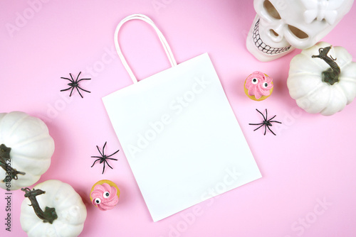 Halloween treat bag mockup. Pink background new season colors. Trick or treat party supplies stationery styled with white skull, pumpkins, black spiders, and spooky cupcakes. Negative copy space.