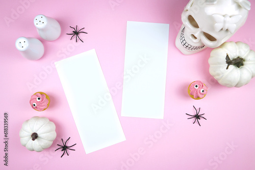 Pink Halloween two 4x9 menu cards mockup. Trick or treat party supplies stationery styled with white skull, pumpkins, black spiders, and spooky cupcakes. Negative copy space. photo