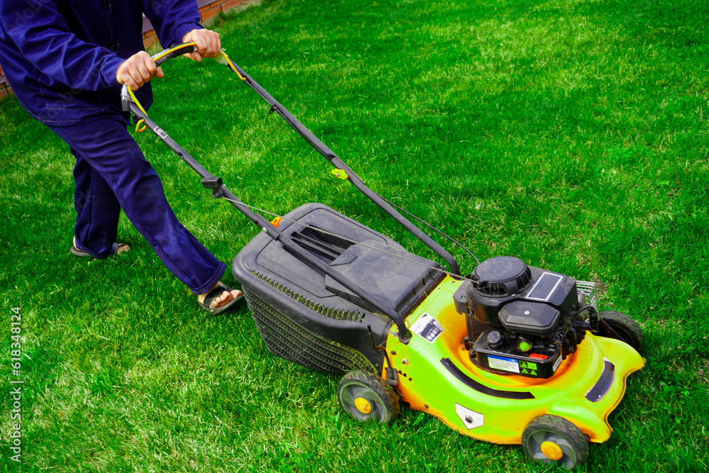 The man is working in the garden. Mowing grass with a lawn mower. The man is working in the garden. Mowing grass with a lawn mower.