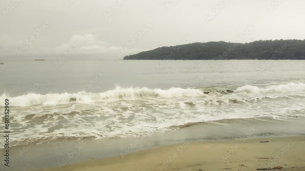 Fototapeta premium waves wash the sand on the beach and a island behind it