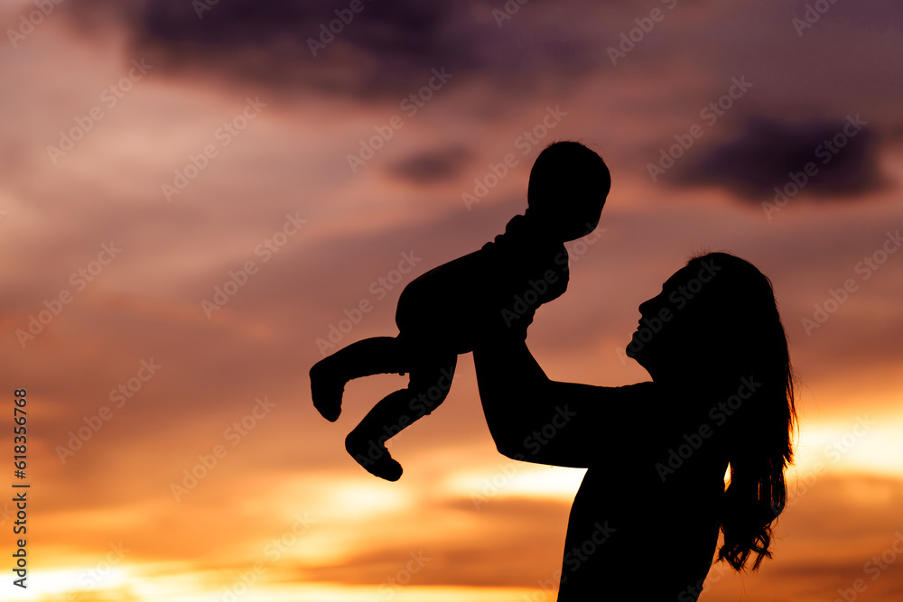 silhouette of mother holding and lifting with infant baby at sunset