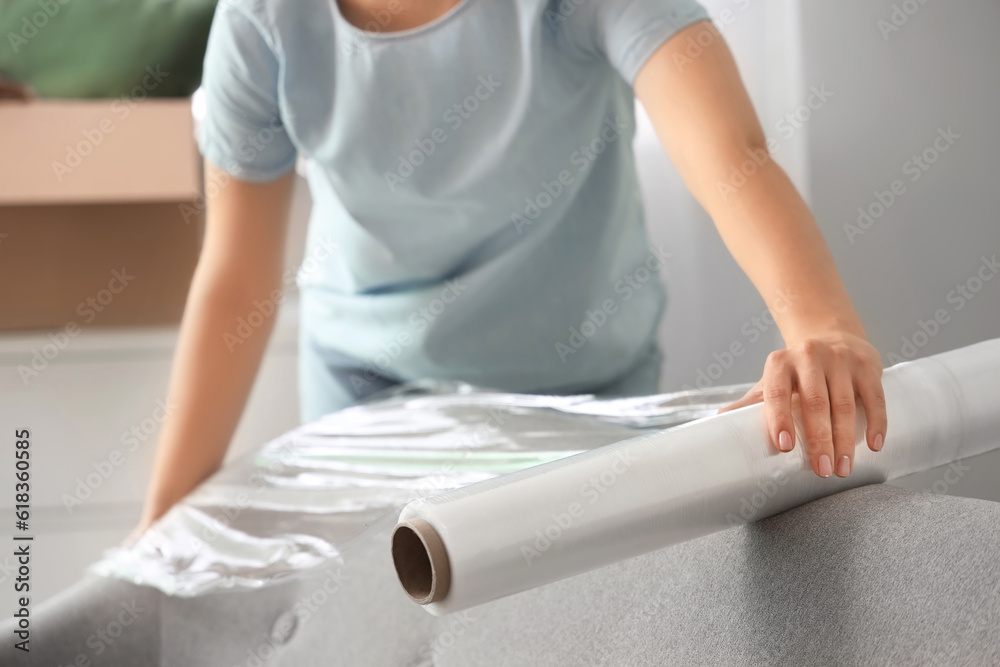 Young woman wrapping sofa with stretch film at home, closeup