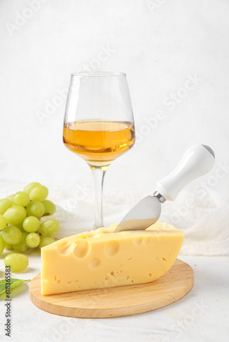Wooden board with tasty Swiss cheese and glass of wine on light background
