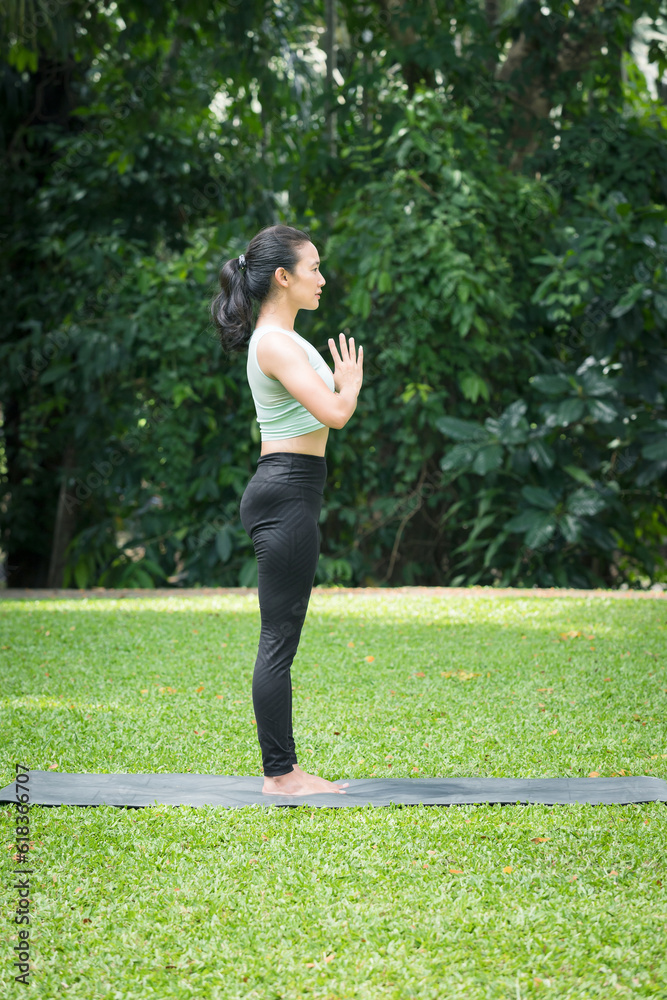 Asian woman practicing yoga in Tree poses, Vrikshasana on the mat in outdoor park.