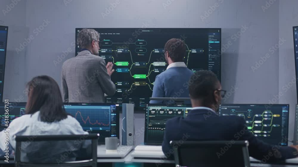 Multiethnic IT technical specialists monitor database server and real-time analysis charts on computers in monitoring office. Software engineers work with blockchain network on big digital screens.