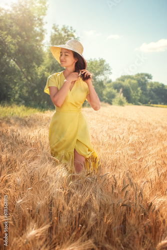 a young woman, in a yellow dress, of white race, walking through a wheat field in a straw hat, at some point stopped and under the rays of the sun, closing her eyes, began to braid her braid.