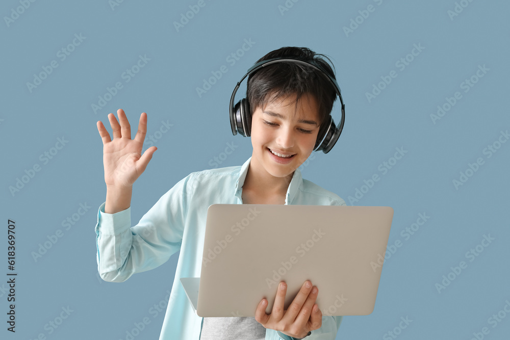 Little boy in headphones with laptop video chatting on blue background Little boy in headphones with laptop video chatting on blue background