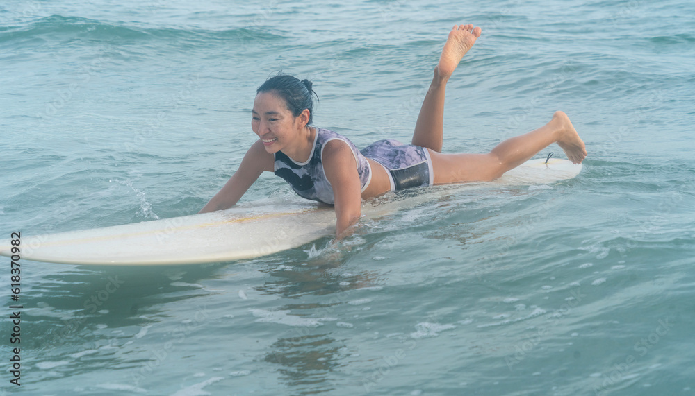 Asian women wearing strong swimsuits hobby surfing waves Lying on the board waiting for the big wave to come from the sea is an exciting water sport on the beach in Thailand.