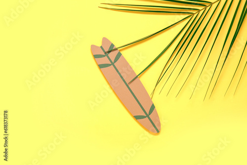 Mini surfboard with palm leaf on yellow background