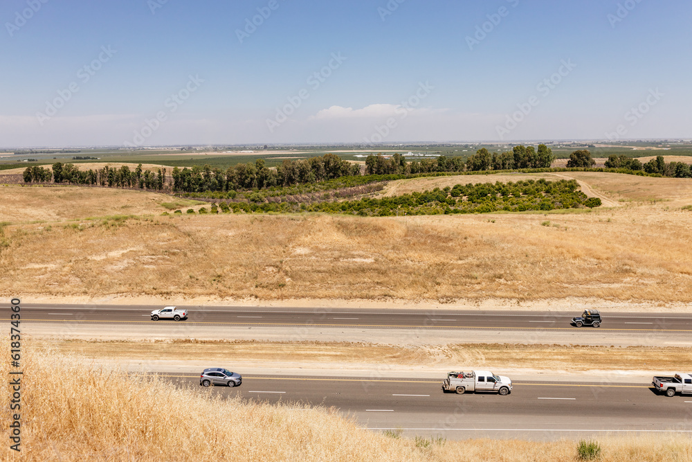 Obraz premium Highway in California, on which cars and trucks drive, among the yellow grass on a sunny day. American landscape from a bird's eye view. Vacation trip