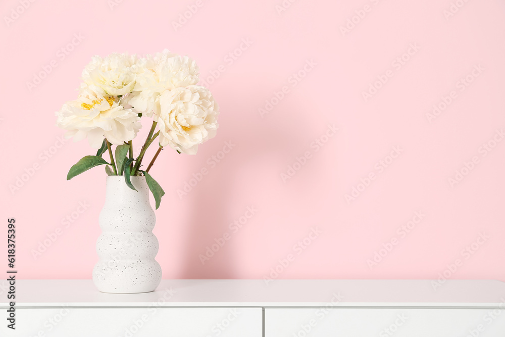 Vase of white peonies on dresser near pink wall Vase of white peonies on dresser near pink wall