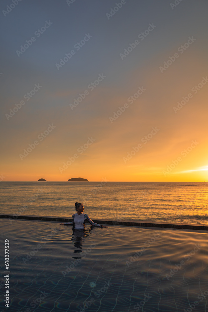 Woman relaxing at the edge of infinity swimming pool at sunset