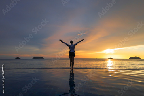 Woman relaxing at the edge of infinity swimming pool at sunset